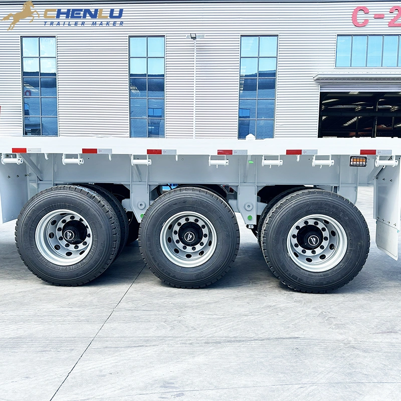 Side view of the three rear axles and wheels on a white flatbed trailer
