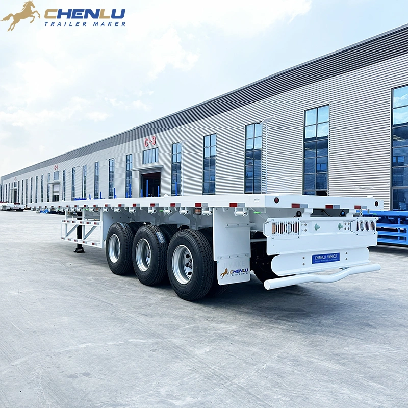White three-axle flatbed trailer viewed from the rear side beside a factory building
