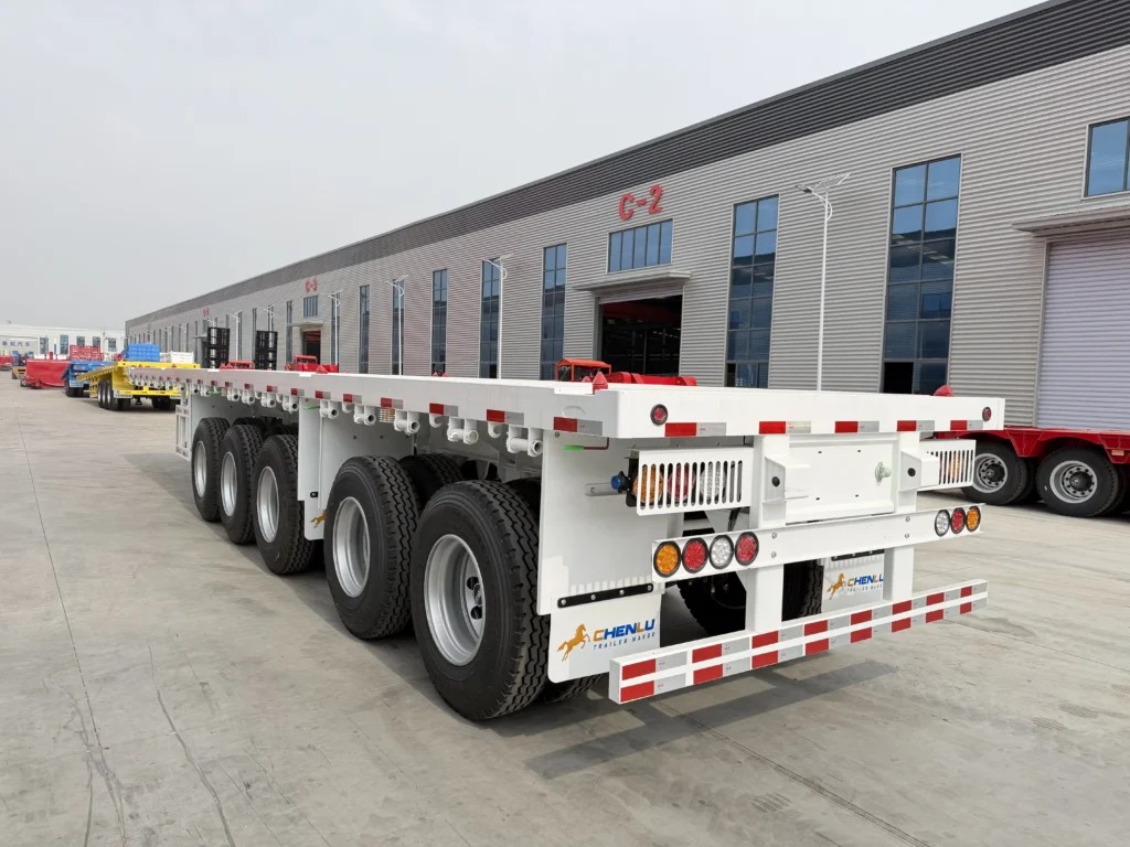 White five-axle flatbed trailer viewed from the rear corner with guarded rear lights