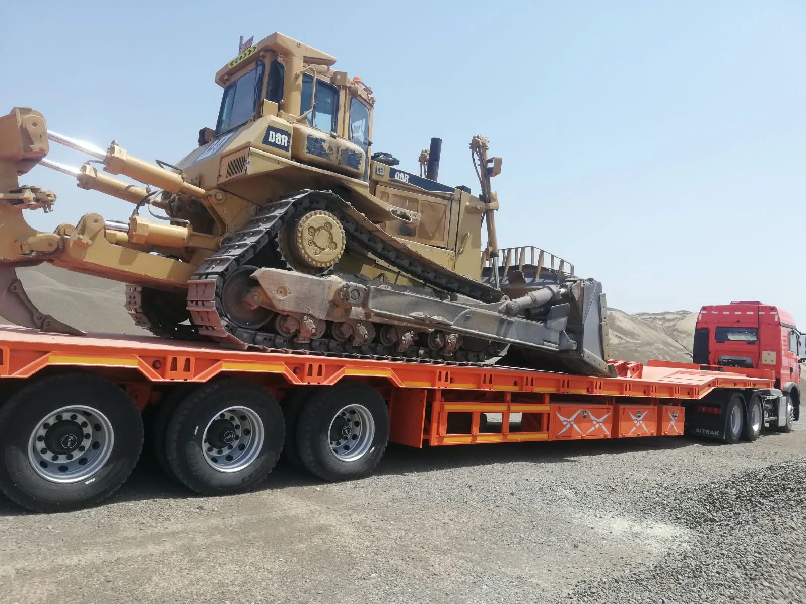 Side view of a three-axle lowbed trailer carrying a tracked bulldozer in Oman