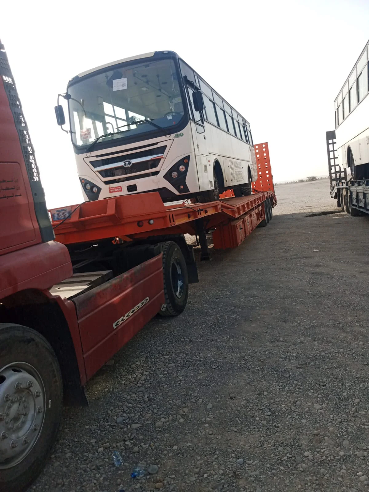 Bus loaded on an orange lowbed trailer with rear loading ramps raised