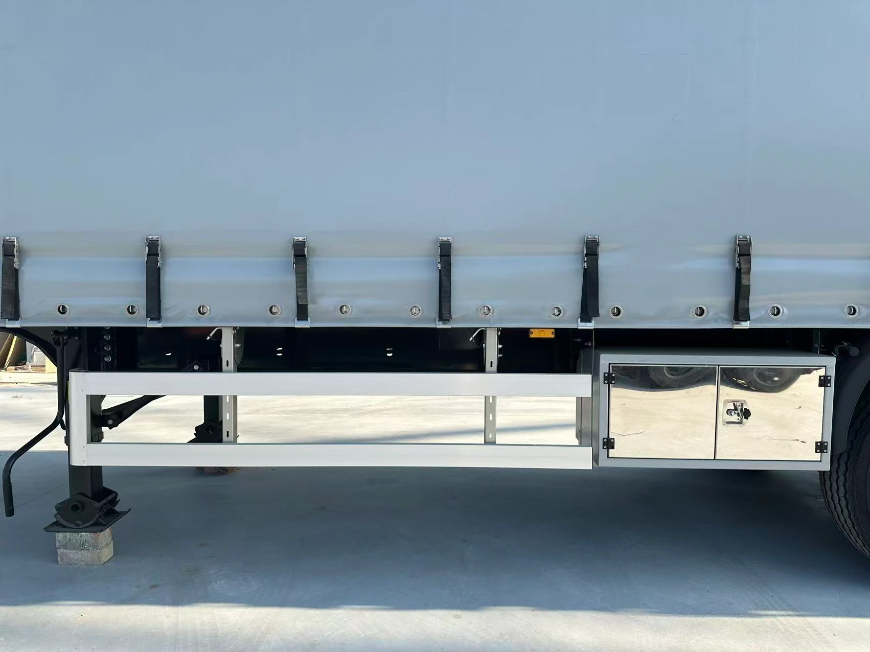 Grey side curtain with black lower buckle straps above the side guard and toolbox