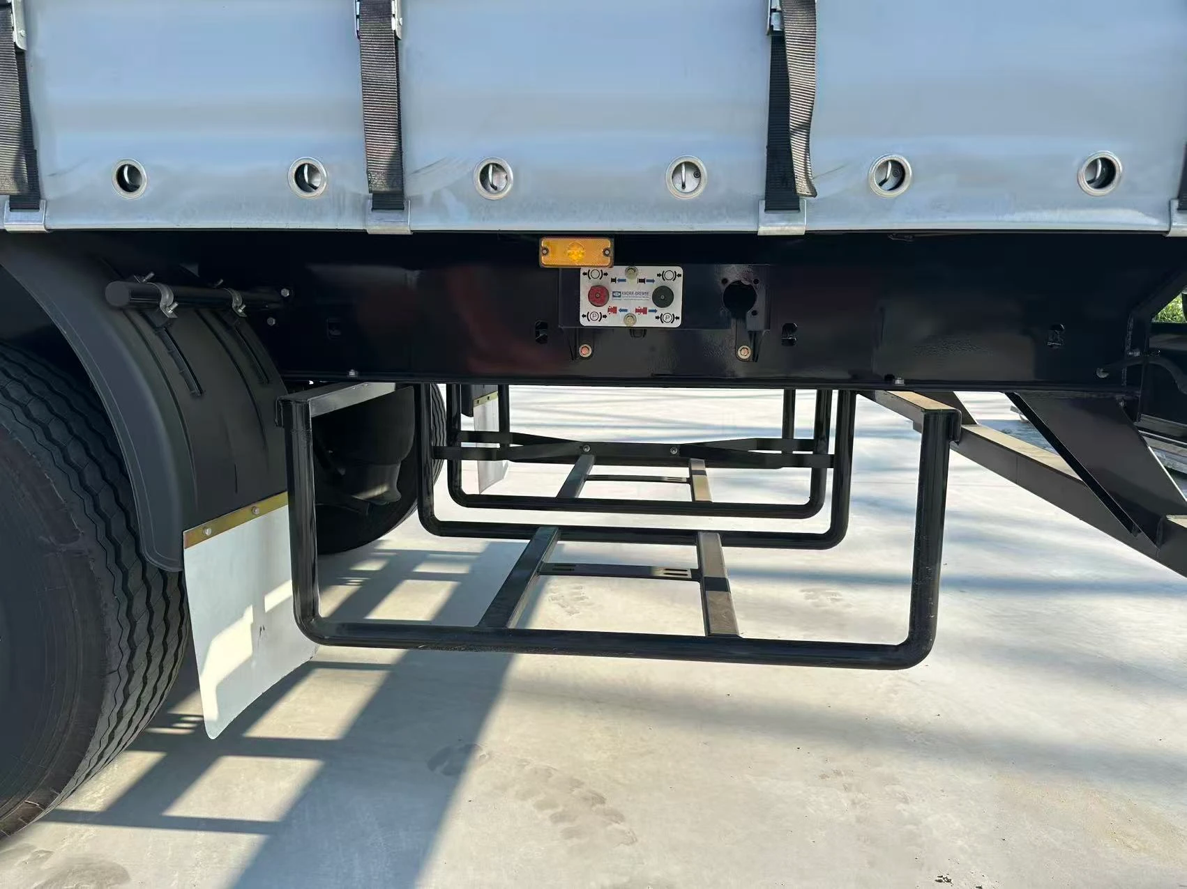 Open tubular storage rack mounted under the side rail near the rear wheels